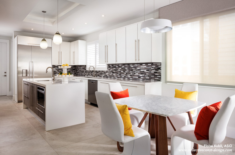 Gloss-white slab-door cabinetry is highlighted by a custom horizontal glass-and-stainless backsplash. The table is topped by matte Carrera Marble on a butterfly maple base, and flanked by four white side chairs.